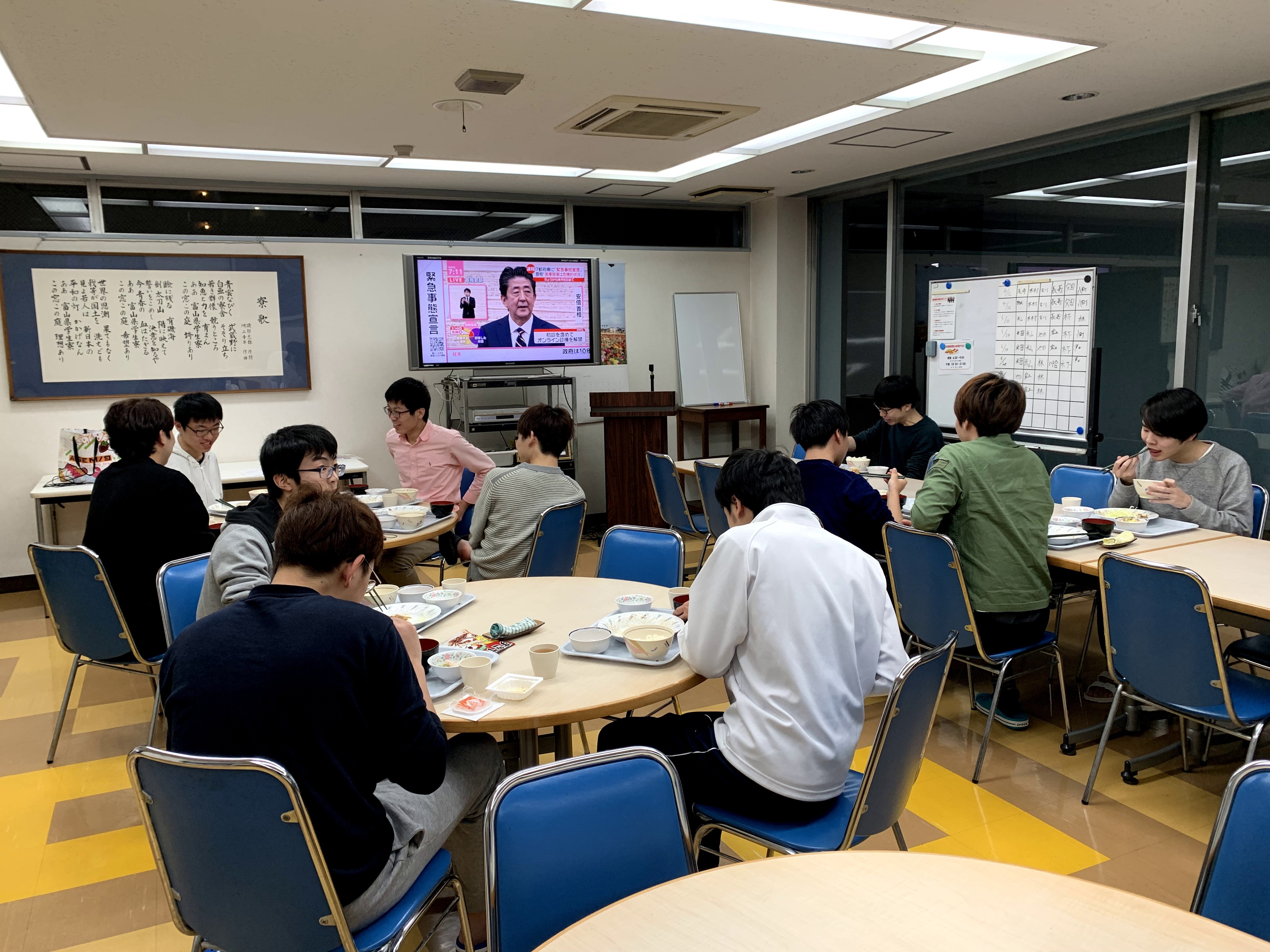食堂で緊急事態宣言を見る寮生たち